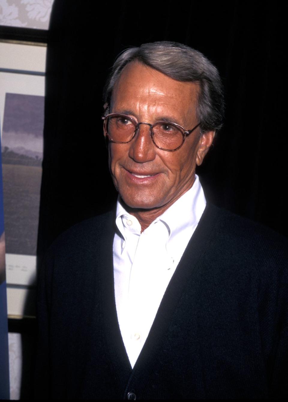 roy scheider wearing a black vest, white dress shirt, and glasses, smiling and looking off camera