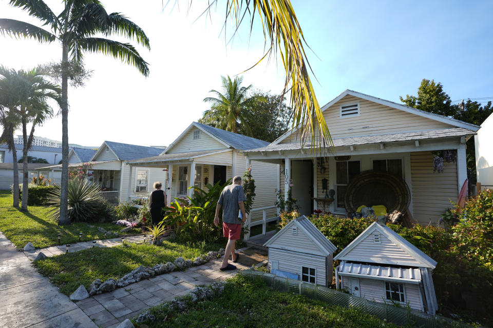 People walk to historic shotgun-style homes in Coral Gables, Fla., bordering the neighborhood of west Coconut Grove, Friday, April 5, 2024. Historically Black West Coconut Grove is a majority Black neighborhood hidden among some of the most affluent areas in Miami that once boomed with sports and economics. (AP Photo/Lynne Sladky)