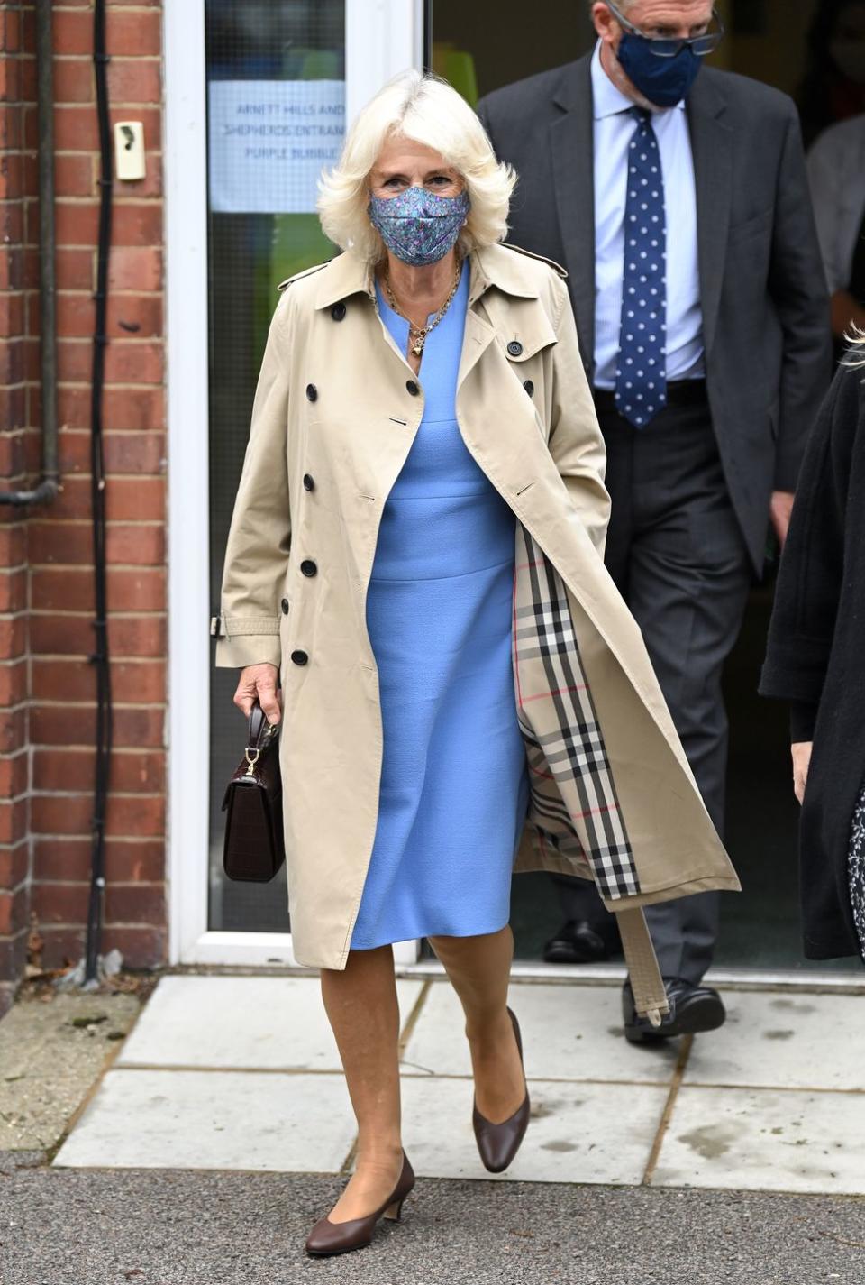 <p>Few garments are quite as characteristically British as <a href="https://www.townandcountrymag.com/style/fashion-trends/g34360257/meghan-markle-kate-middleton-royal-trench-outfit-photos/" rel="nofollow noopener" target="_blank" data-ylk="slk:the classic Burberry trench;elm:context_link;itc:0;sec:content-canvas" class="link ">the classic Burberry trench</a>. Camilla embraced this preppy look by pairing it with a powder blue dress and matching mask. </p>