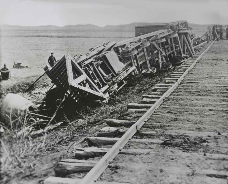 derailed train lies on its side next to train tracks