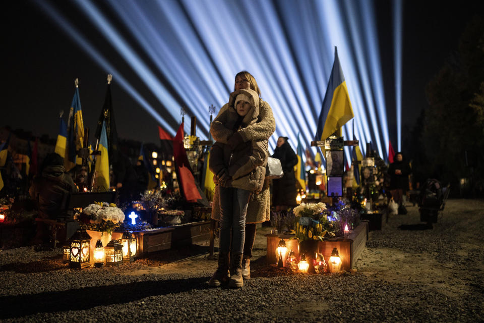 A woman and her daughter listen to a prayer for fallen soldiers at Lviv cemetery, western Ukraine, on Thursday, Feb. 23, 2023. (AP Photo/Petros Giannakouris)