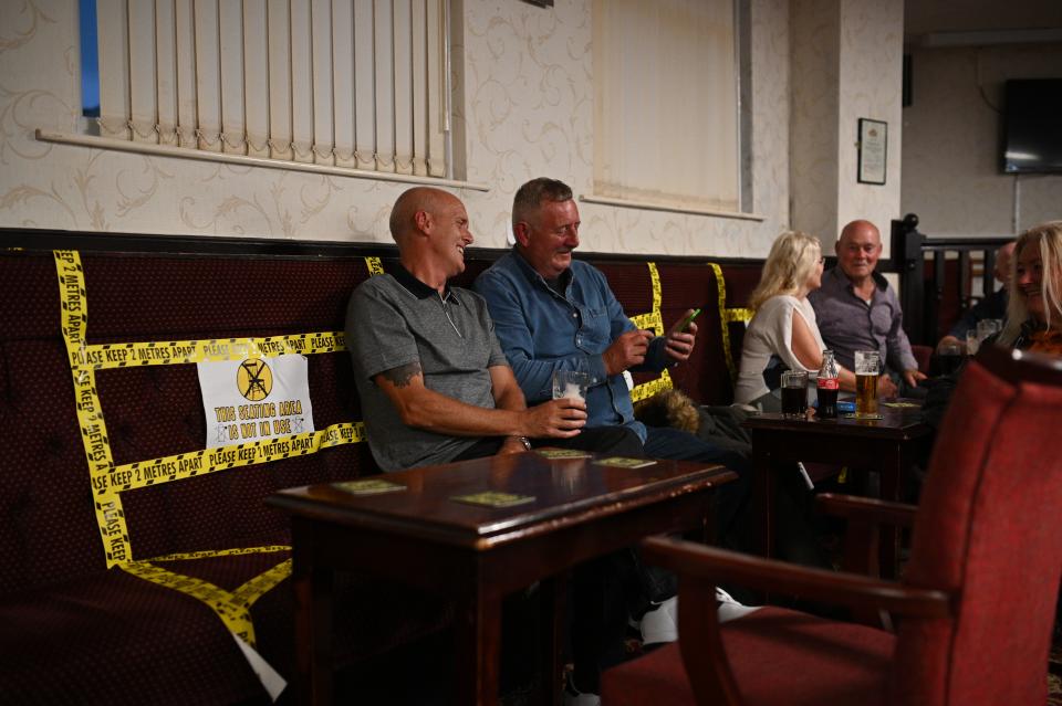 People enjoy a drink with yellow tape on the seats aiding social distancing inside the Burnley Miners Working Men's Social Club in Burnley, northwest England, on July 4, 2020, as restrictions are further eased during the novel coronavirus COVID-19 pandemic. - Pubs in England reopen on Saturday for the first time since late March, bringing cheer to drinkers and the industry but fears of public disorder and fresh coronavirus cases. (Photo by Oli SCARFF / AFP) (Photo by OLI SCARFF/AFP via Getty Images)