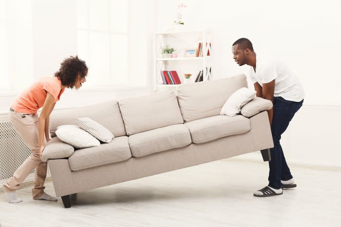 A man and woman move a sofa into position in a large living area.