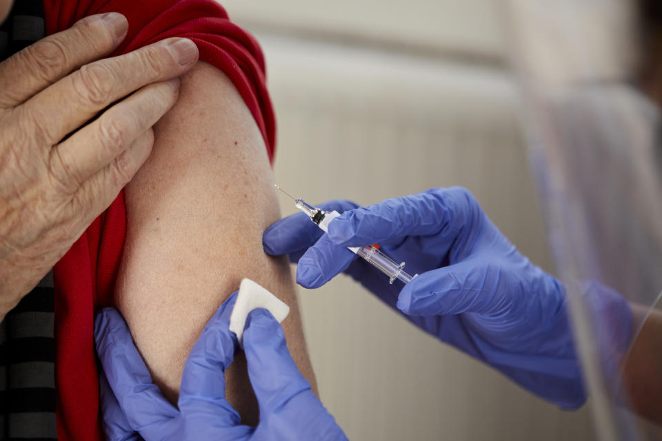 A person is receiving an injection in their upper arm with medical personnel administering the shot