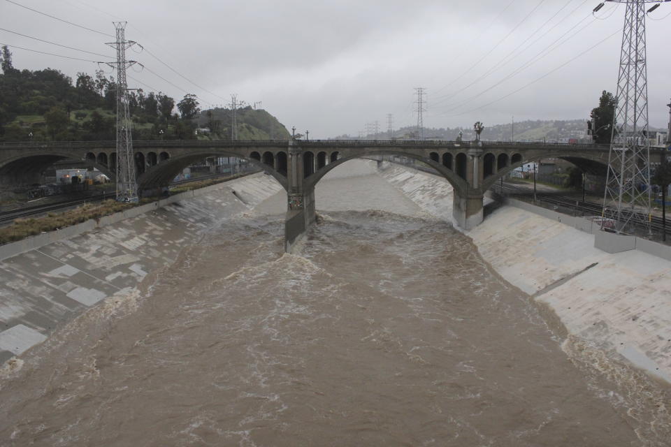 The rain-swollen Los Angeles River flows near downtown Los Angeles on Saturday, Feb. 25, 2023, as a powerful storm pounds Southern California. The National Weather Service said periods of heavy rain and mountain snow would continue before winding down by evening. (AP Photo/John Antczak)