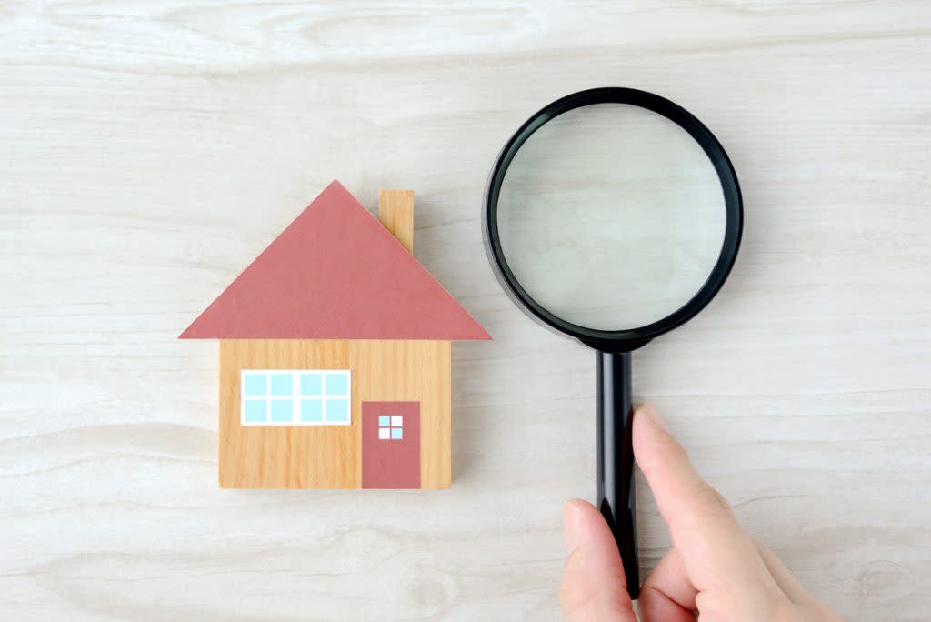 A wooden house has a magnifying glass next to it meant to represent a house inspection.