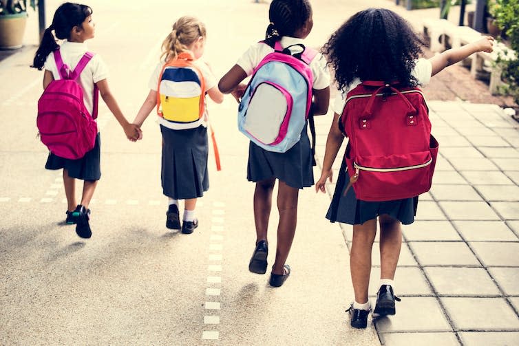 Children in school uniforms walk outside with backpacks.