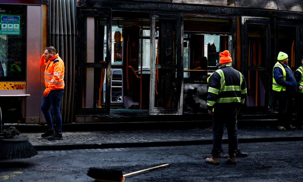 Workers clear a burnt-out tram