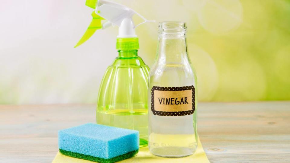 How to clean a waffle iron: concept of chemical-free household cleaning products. Use natural distilled white vinegar in a spray bottle to remove stains. Tools on wooden table, green bokeh background, copy space.