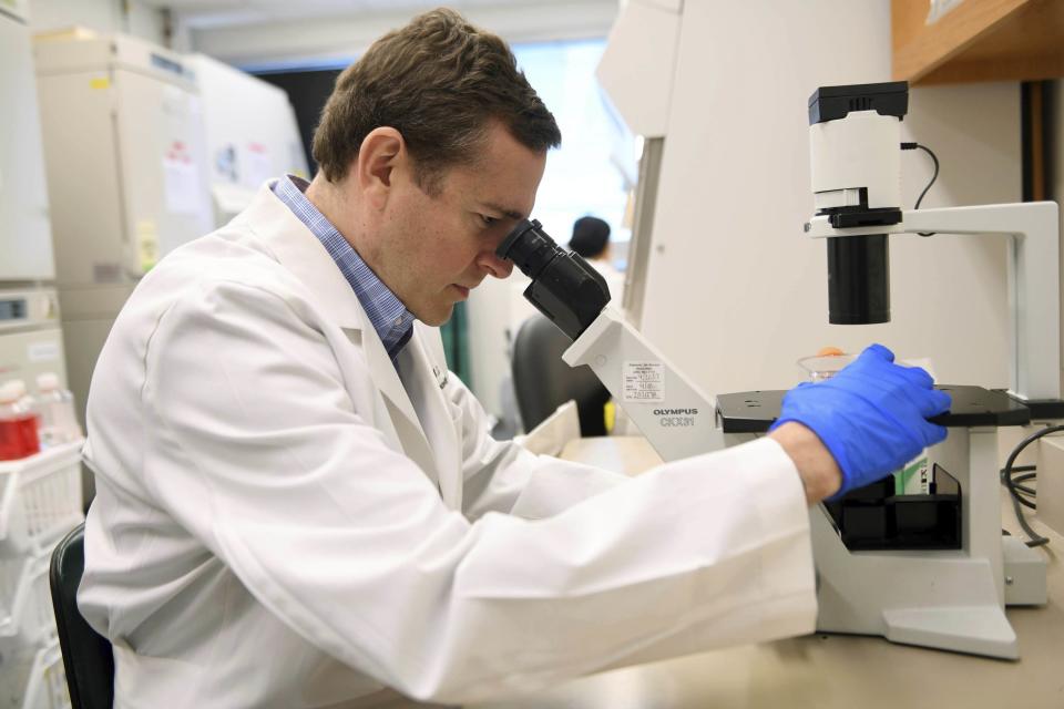 In this Aug. 5, 2019 photo provided by Children’s Of Alabama, Dr. Gregory Friedman, a childhood cancer specialist, looks through a microscope at a laboratory in Birmingham, Ala. Friedman is leading a study to treat a deadly type of childhood cancer with a treatment that involves infusing viruses directly into the brain to spur an immune system response to the cancerous cells. (Denise McGill/Children’s Of Alabama via AP)