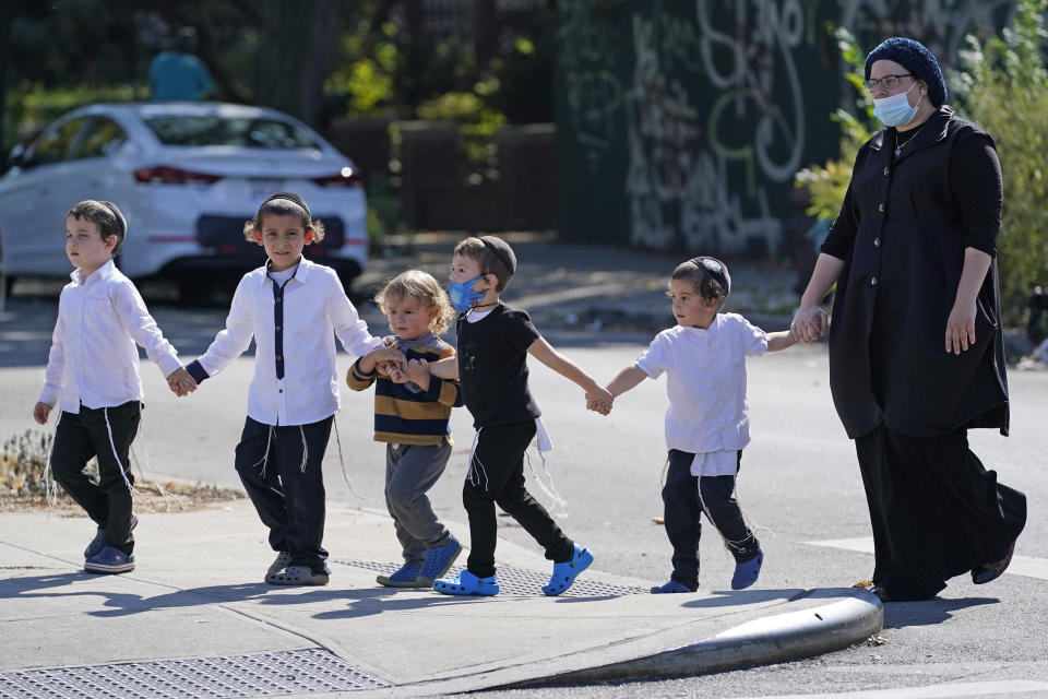 A woman and a group of young children cross a busy street, Monday, Sept. 28, 2020, in the Midwood neighborhood of the Brooklyn borough of New York. New York Gov. Andrew Cuomo raised alarms Monday about the emergence of a handful of coronavirus hot spots in New York, saying just 10 ZIP codes represented more than a quarter of the state's new infections in recent testing. Midwood is one of the neighborhoods experiencing an uptick in virus cases. (AP Photo/Kathy Willens)