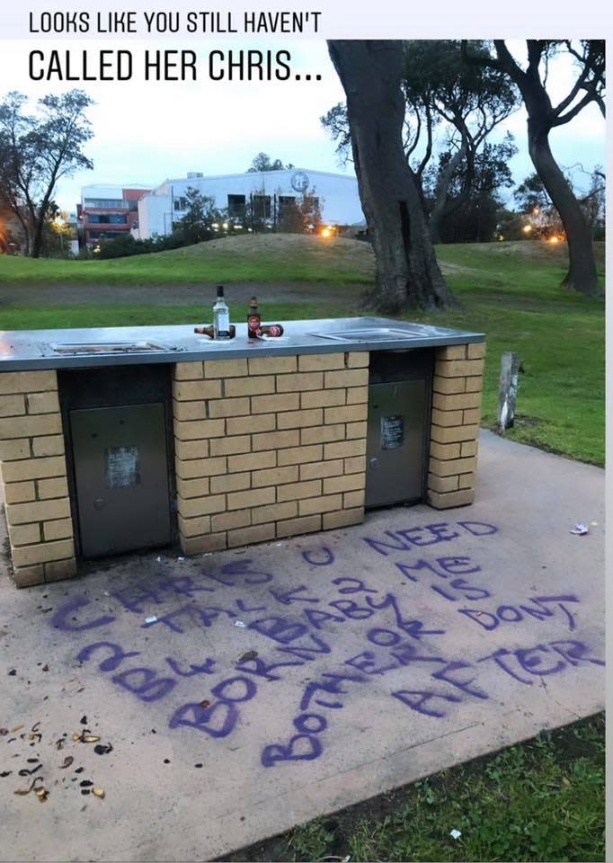 Purple graffiti is seen on a paved area next to a public barbecue. 