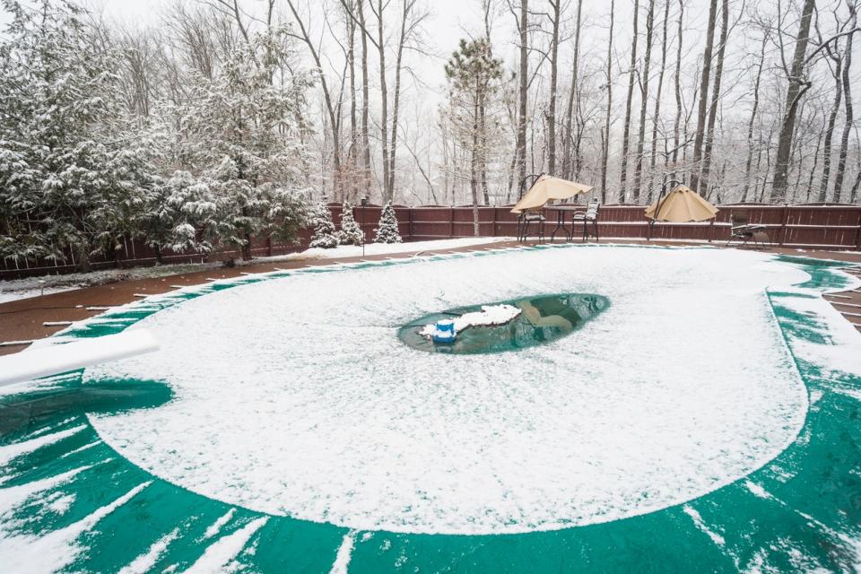 Snow-is-melting-in-the-center-of-a-swimming-pool-cover-surrounded-by-winter-trees