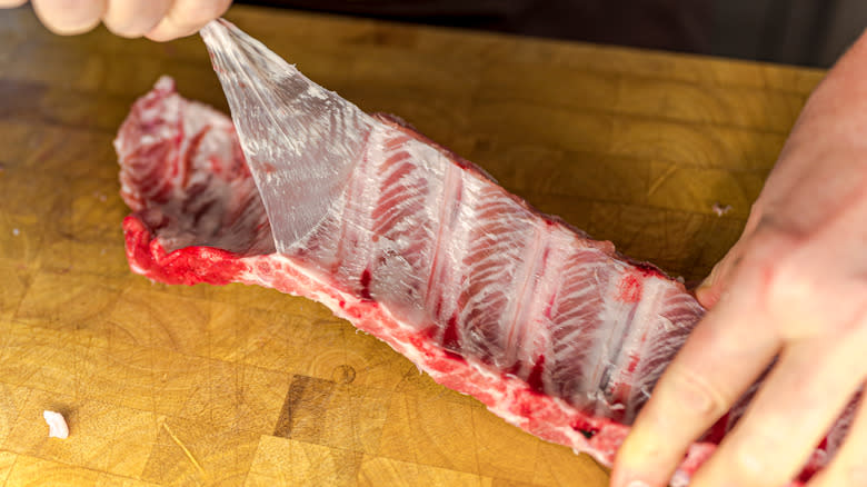 Hands removing silver skin from raw beef