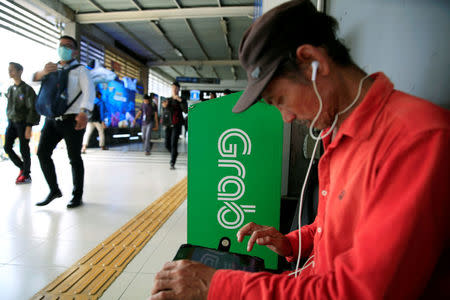 A passenger sits next to Grab corner sign as he waits for a Grab bike at Sudirman train station in Jakarta, Indonesia, March 26, 2018. REUTERS/Beawiharta