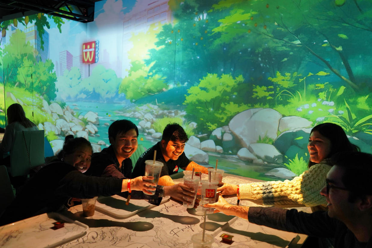 A group of diners cheers with their cups of Sprite over a white table with a projected map on it. (Samantha Kubota / TODAY)