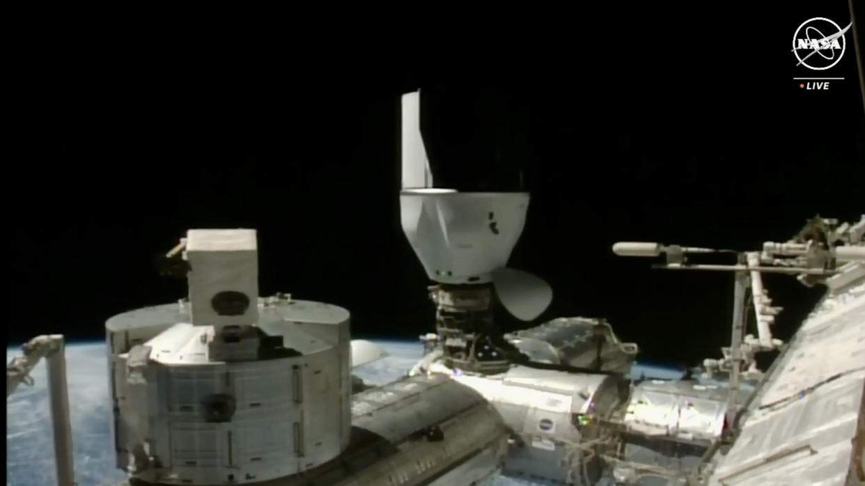  A spacecraft capsule is docked upside down to the upward docking port of a chrome space station module. 