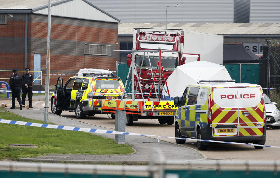 Police officers attend the scene after a truck, in rear, was found to contain a large number of dead bodies, in Thurrock, South England, early Wednesday Oct. 23, 2019. Police in southeastern England said that 39 people were found dead Wednesday inside a truck container believed to have come from Bulgaria. (AP Photo/Alastair Grant)