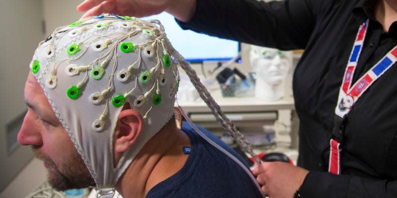 Former NHL player Bryan Muir wears an EEG cap being adjusted by a concussion researcher.