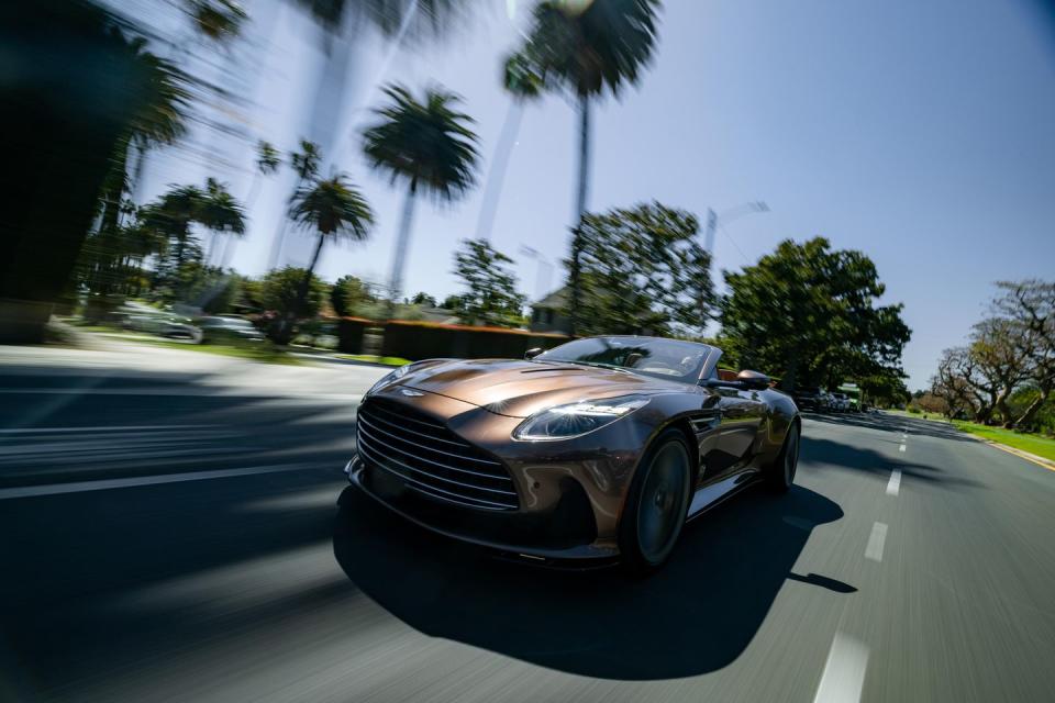 a brown aston martin db12 volante driving on a road