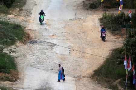 A woman crosses a street as people ride motorbikes at a main road in Semboja district, Kutai Kertanegara regency