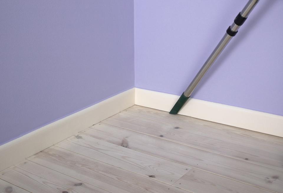 using vacuum cleaner extension to remove dust between skirting board and floorboard