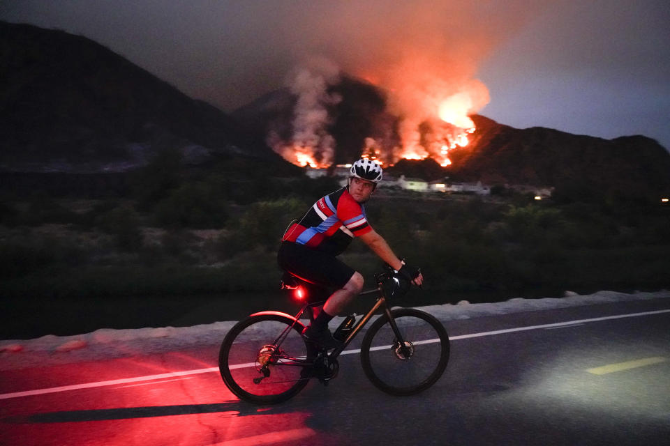 A cyclist rides along a trail as the Ranch Fire burns, Thursday, Aug. 13, 2020, in Azusa, Calif. Heat wave conditions were making difficult work for fire crews battling brush fires and wildfires across Southern California. (AP Photo/Marcio Jose Sanchez)