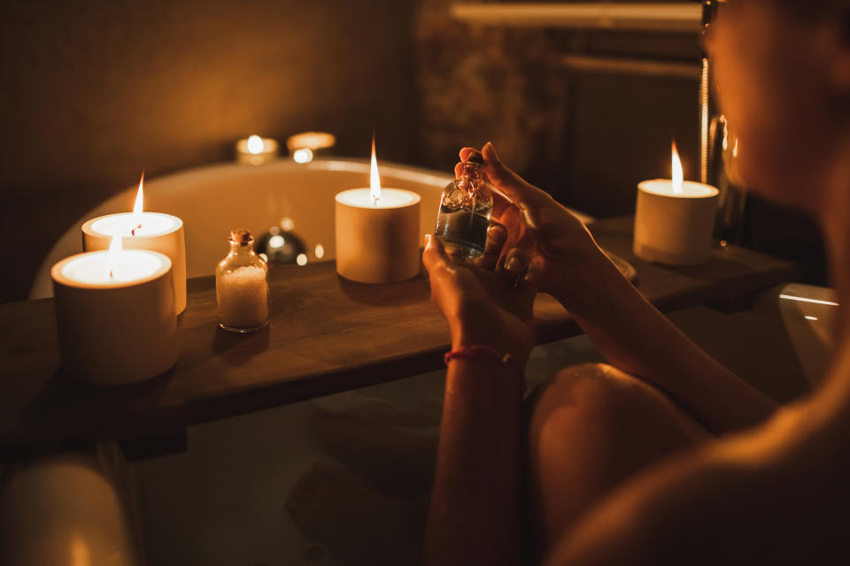 Person holding a small glass bottle while sitting in a candlelit bathtub