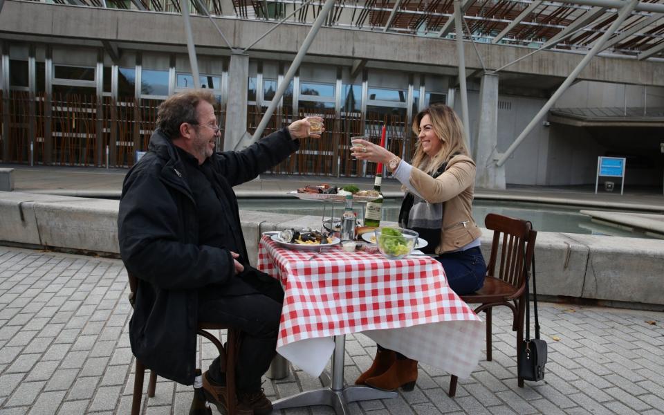 Pierre Levicky owner of Chez Jules restaurant in Edinburgh alongside Kasia Panisco as they stage a protest by having a meal outside the Scottish Parliament in Edinburgh after a range of new restrictions to combat the rise in coronavirus cases came into place in Scotland - PA
