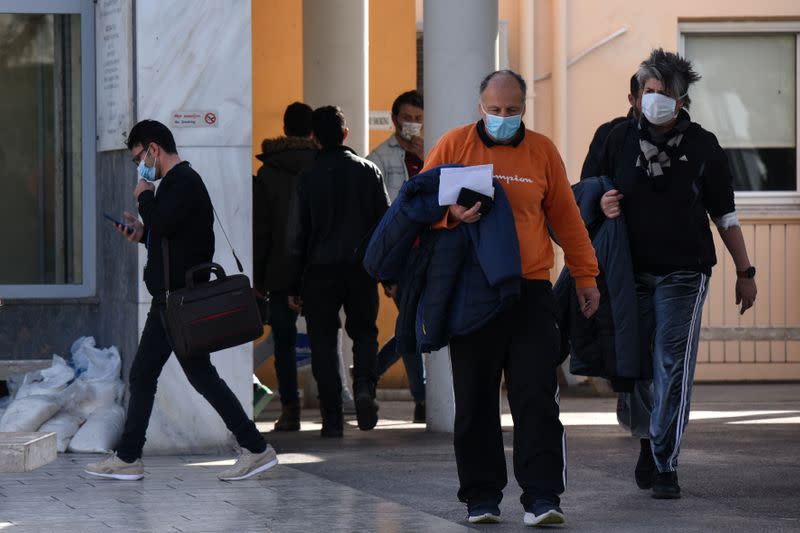 People wearing protective face masks sit outside the AHEPA hospital, where the first confirmed coronavirus case is being treated, in Thessaloniki