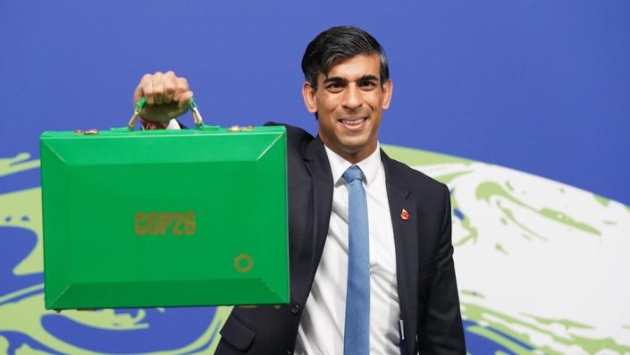 Rishi Sunak holds up treasury briefcase painted green in front of COP26 logo of world