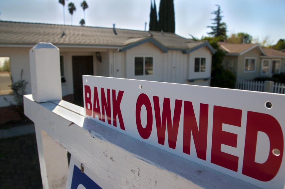 A foreclosed home shows a bank owned for sale sign.