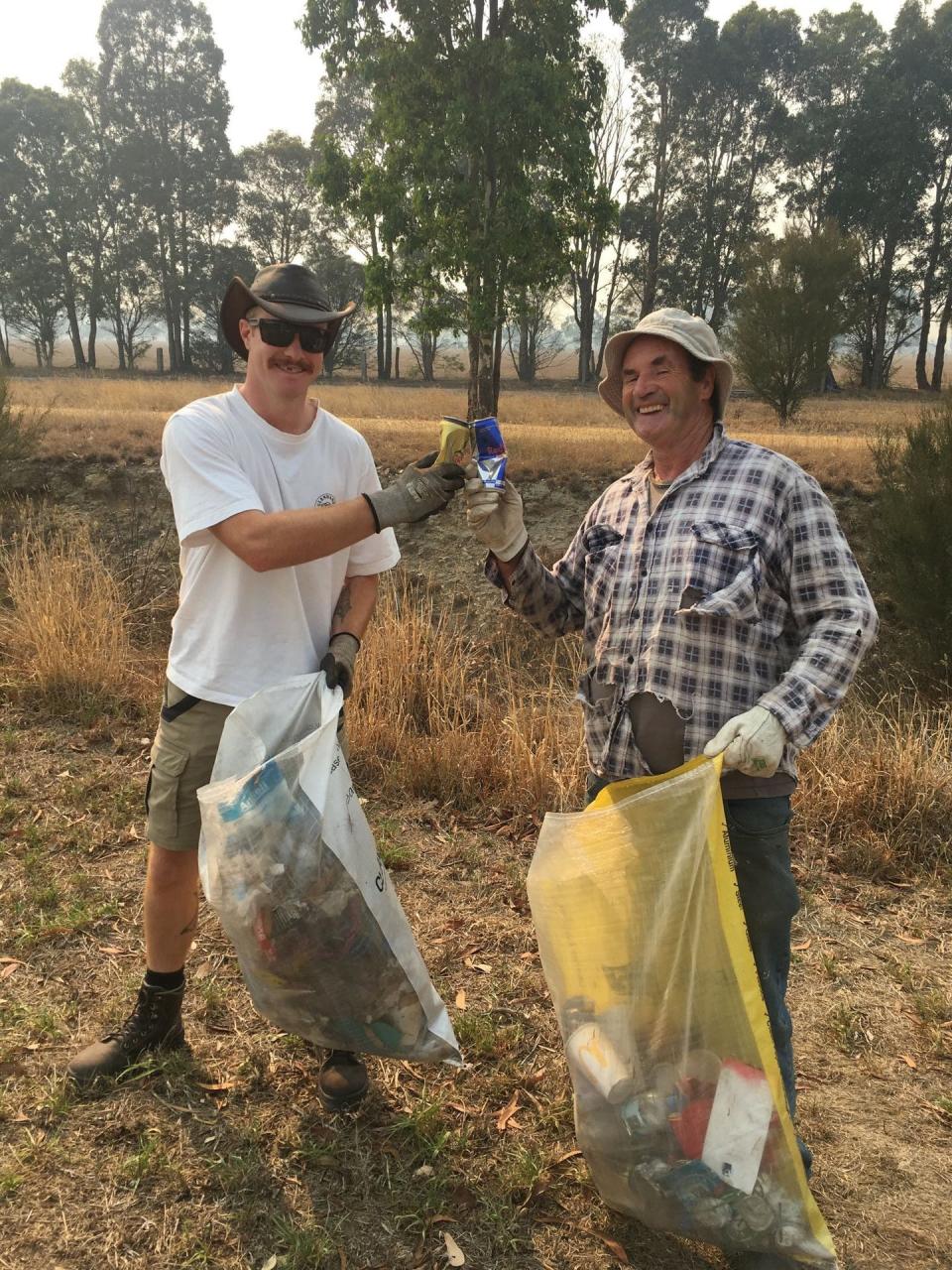 Two smiling men hold bags of rubbish