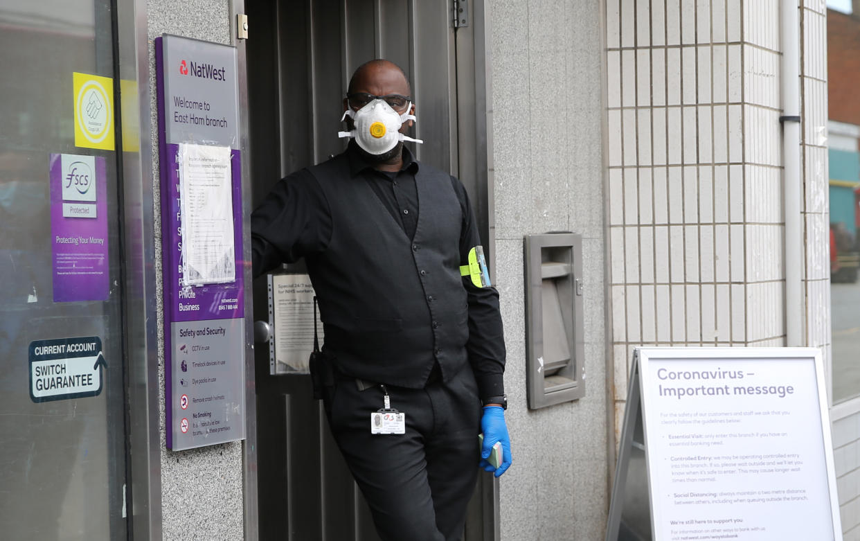 A security man wearing protective personal equipment controls a queue outside a branch of Natwest Bank in East Ham, east London, as the UK continues in lockdown to help curb the spread of the coronavirus. Picture date: Tuesday April 28, 2020. 