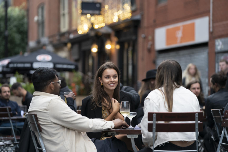 Members of the public are seen at a bar in Manchester's Northern Quarter, England, Saturday July 4, 2020. England is embarking on perhaps its biggest lockdown easing yet as pubs and restaurants have the right to reopen for the first time in more than three months. In addition to the reopening of much of the hospitality sector, couples can tie the knot once again, while many of those who have had enough of their lockdown hair can finally get a trim. (AP Photo/Jon Super)