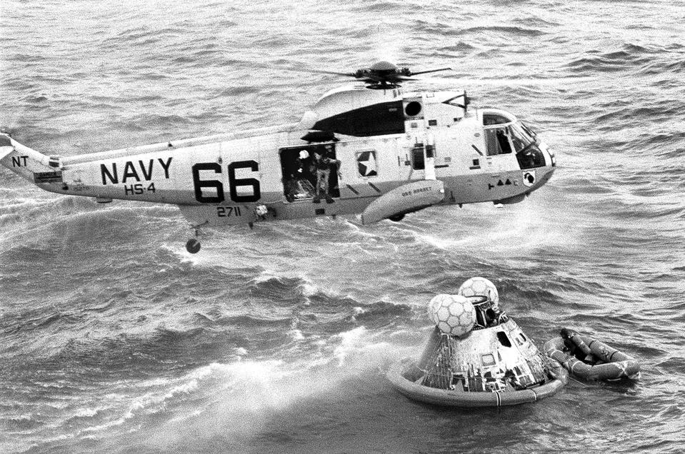 In this July 24, 1969 photo from the U.S. Navy, Navy UDT swimmer Clancy Hatleberg prepares to jump from a helicopter into the water next to the Apollo 11 capsule after it splashed down in the Pacific Ocean, to assist the astronauts into the raft at right. (Milt Putnam/U.S. Navy via AP)