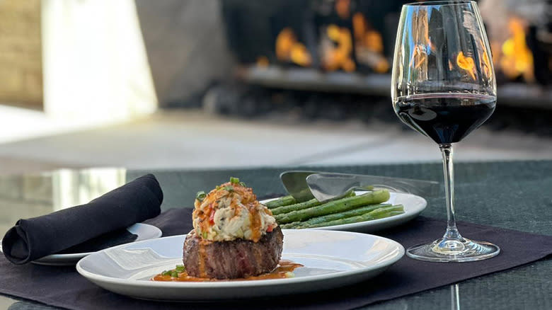 steak on white plate with wine and fire in background