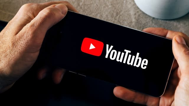 Person holds a phone displaying a YouTube logo