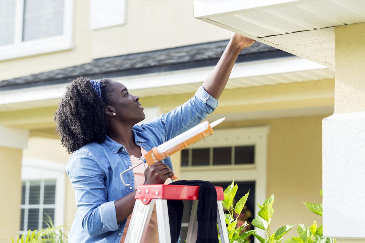 Woman on a ladder doing house repairs outside