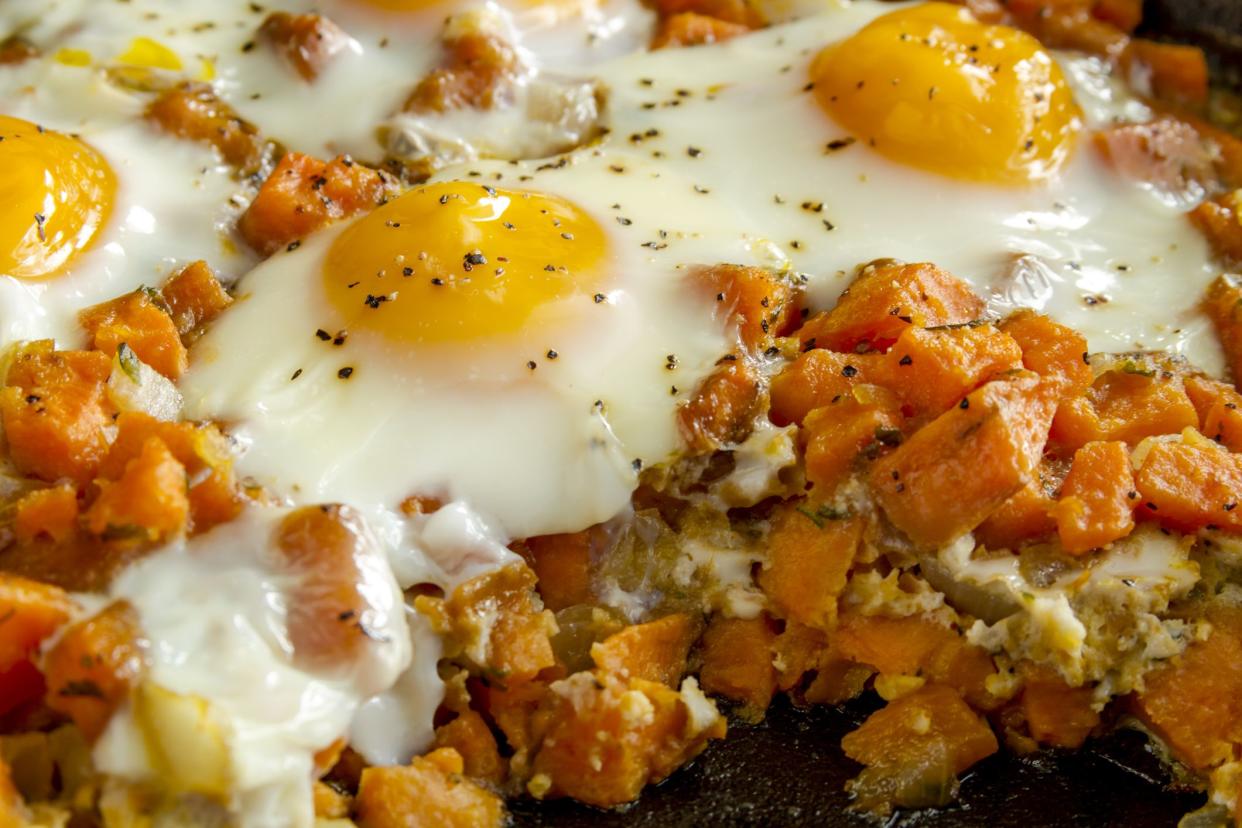 Close up of cast iron skillet filled with fried eggs and sweet potato hash