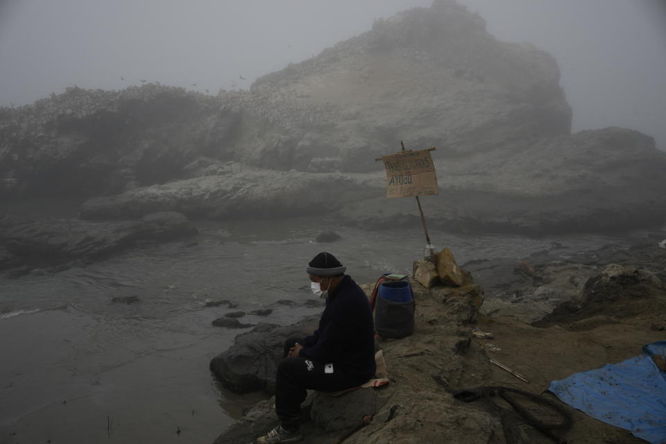 Fisherman Walter de la Cruz sits on the oil stained Cavero Beach, unable to fish after a spill in the Ventanilla district of Callao, Peru, Friday, Jan. 21, 2022. The oil spill on the Peruvian coast was caused by the waves from an eruption of an undersea volcano in the South Pacific nation of Tonga. (AP Photo/Martin Mejia)