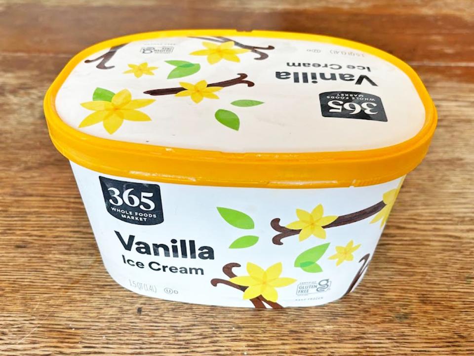 A white carton of ice cream with graphics of vanilla beans and flowers on it. The lid has a yellow band and the carton has a 365 logo on it