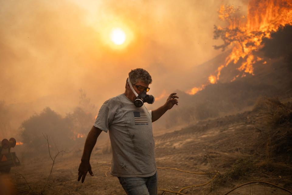 A wearing breathing protection man reacts as a fire burns into the village of Gennadi on the Greek Aegean island of Rhodes (AFP via Getty Images)