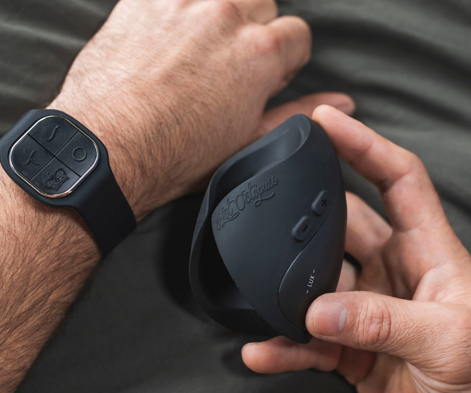 A close up of a man's arm wearing a black silicone watch on the left with his right hand holding a black silicone Pulse Hot Octopuss toy