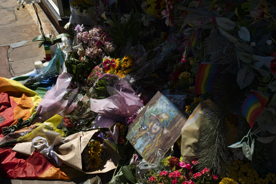 A small painting of store owner Laura Ann Carleton is seen surrounded by flowers and Pride flags placed on a memorial outside her store in the Studio City section of Los Angeles, Wednesday, Aug. 23, 2023. Authorities say a 27-year-old man was killed by California sheriff's deputies over the weekend after he fatally shot Carleton, outside her store in Cedar Glen, Calif., roughly 60 miles (96 kilometers) east of downtown Los Angeles. Investigators determined that prior to the shooting the suspect tore down a Pride, or rainbow, flag that was hanging in front of the store and yelled many homophobic slurs toward Carleton. (AP Photo/Richard Vogel)