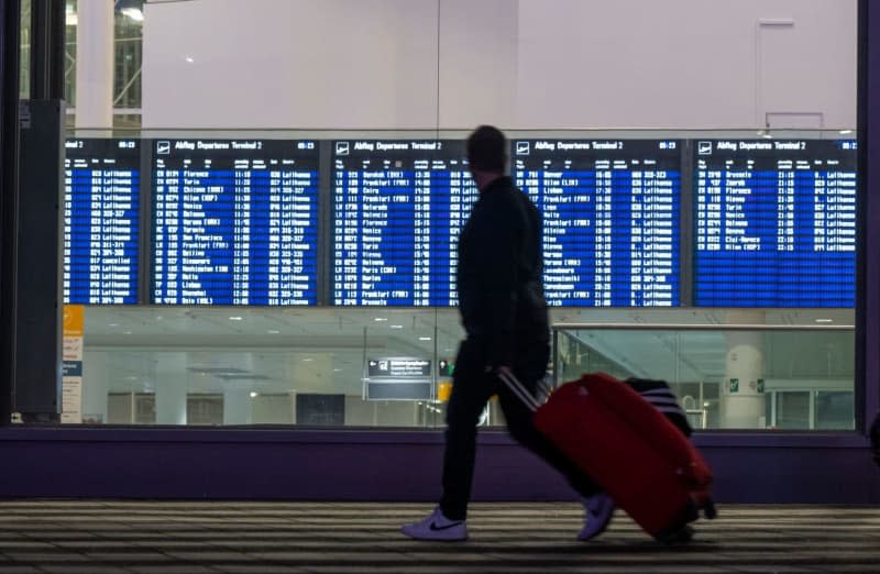 A man with a suitcase walks past a display board for departures at Munich Airport. The cabin crew union Ufo has called on around 19,000 airline employees to go on strike. All Lufthansa departures from Munich will be on strike from 4 a.m. to 11 p.m. Peter Kneffel/dpa