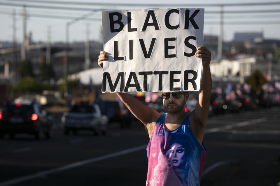A Black Lives Matter supporter holds a sign as supporters of President Donald Trump attend a rally and car parade Saturday, Aug. 20, 2020, from Clackamas to Portland, Ore. (AP Photo/Paula Bronstein)
