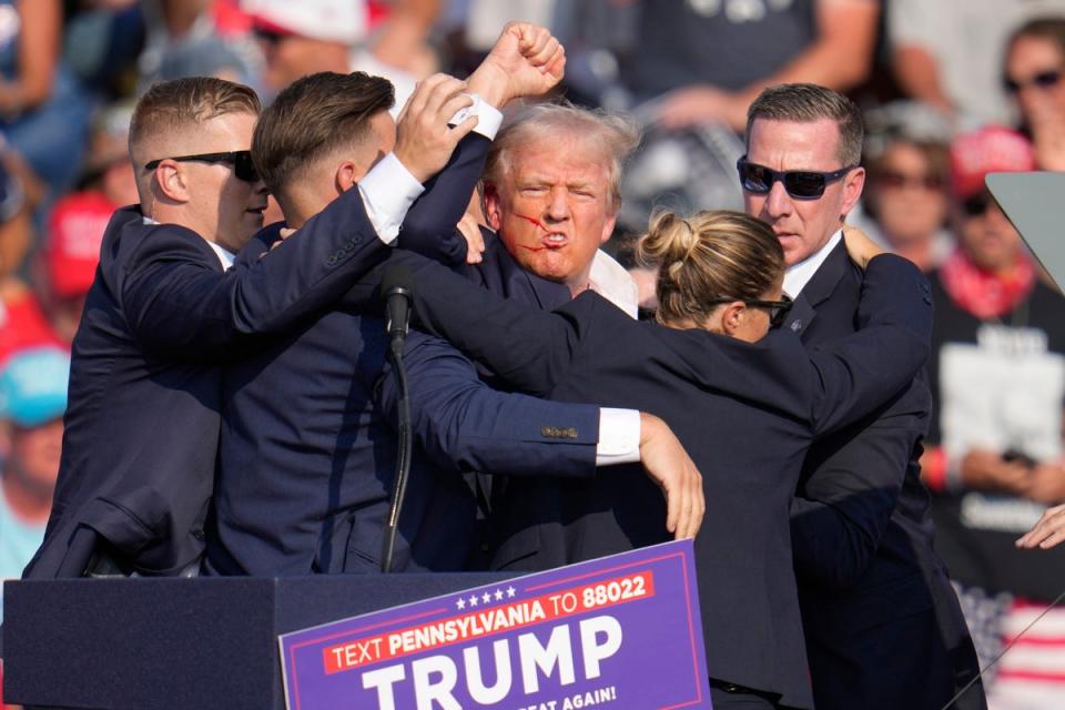 An injured Donald Trump surrounded by agents on stage following the assassination attempt (AP)