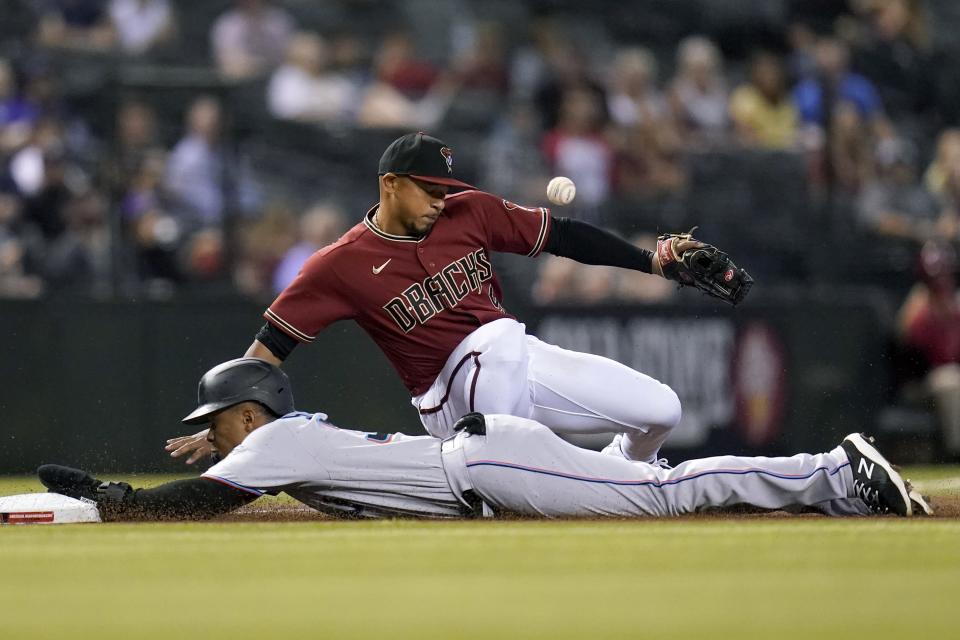 Arizona Diamondbacks third baseman Eduardo Escobar, back, misses the ball as Miami Marlins' Magneuris Sierra, front, slides safely into third base, advancing on a fly ball, during the seventh inning of a baseball game Wednesday, May 12, 2021, in Phoenix. (AP Photo/Ross D. Franklin)