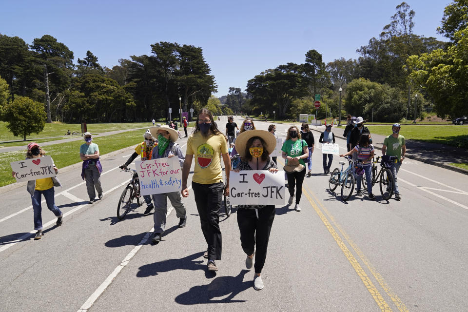 A group of people march along John F. Kennedy Drive in Golden Gate Park to celebrate the one-year anniversary of the roadway being closed to cars, Wednesday, April 28, 2021, in San Francisco. At the start of the pandemic, San Francisco closed off parts of a major beachfront highway and Golden Gate Park to cars so that people had a safe place to run and ride bikes. Open space advocates want to keep those areas car-free as part of a bold reimagining of how U.S. cities look. But opponents decry the continued closures as elitist, unsafe and nonsensical now that the pandemic is over and people need to drive again. (AP Photo/Eric Risberg)